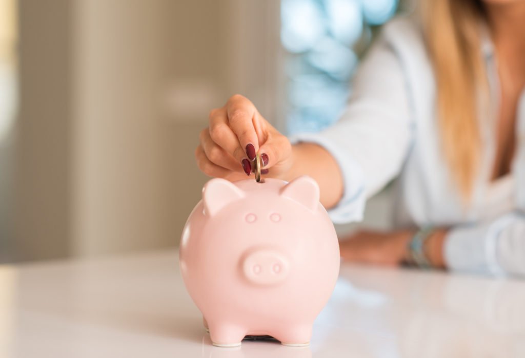 Beautiful young woman hands holding a coin investing in to a piggy bank at home. Business concept.